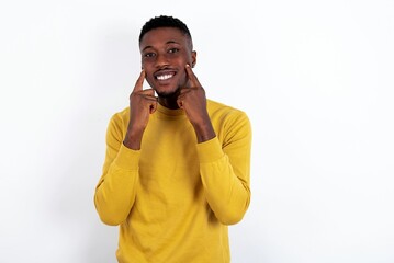 Wall Mural - Strong healthy straight white teeth. Close up portrait of happy young handsome man wearing yellow sweater over white background with beaming smile pointing on perfect clear white teeth.