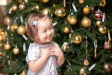 Happy Kind Child Girl With Down Syndrome Smiling Near The Christmas Tree