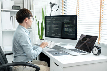 Male programmer is programming to develop program app and website of corporate while working to checking program code and debugging on multiple screen at modern software office