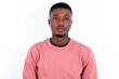© Jihan - Joyful young handsome man wearing pink sweater over white background looking to the camera, thinking about something. Both arms down, neutral facial expression.