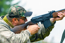 A Man Takes Aim And Shoots A Combat Carbine Or Guns In Blurry Focus At Targets In A Shooting Range. View Of A Shooting Hunter During Hunting.