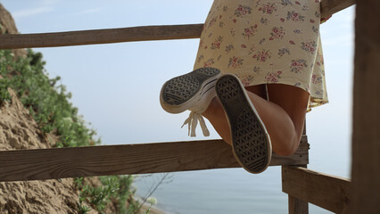 Wall Mural - Slim girl legs wearing sneakers at ocean close up. Woman leaning on staircase.