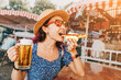 canvas print picture - Happy girl drinking beer and eating traditional german bratwurst - hotdog at funfair and street food festival. National cuisine and biergarten concept