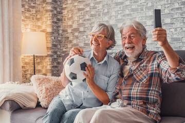 Happy couple of seniors or football fans watching soccer on tv and celebrating victory at home. Family, sports and entertainment concept..