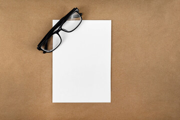 Poster - A notebook with glasses in a minimal style top view isolated on brown background of recycled craft vintage paper