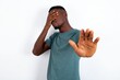 young handsome man wearing green T-shirt over white background covers eyes with palm and doing stop gesture, tries to hide. Don't look at me, I don't want to see, feels ashamed or scared.