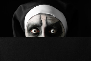 Wall Mural - Scary devilish nun hiding on black background, closeup. Halloween party look