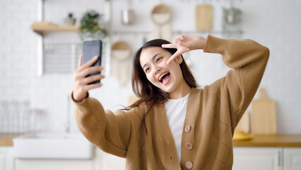 Poster - Pretty young asian female smile and stand at kitchen room. She having fun taking selfie and video call talking with her friend