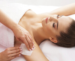 Wall Mural - Hair removal, beauty and health concept. A young girl is getting an epilation procedure. A processional beauty worker is making depilation with hot wax.