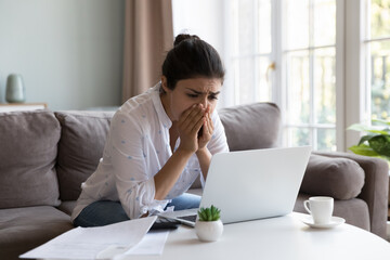 Indian woman feels desperate due to financial problem, huge bank debt, unpaid household domestic utility bills sit on sofa looks at laptop screen read bad news about bankruptcy, blocked e-bank account