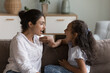 © fizkes - Young Indian mother and cute daughter practicing speaking together, doing vocal exercises seated on sofa at home, therapist logopaedist correct pronunciation of preschooler girl, help to stutter kid