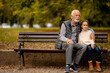 Grandfather spending time with his granddaughter on bench in park on autumn day