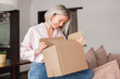 © Tatyana Gladskih - woman sitting on couch at home opening carton box received parcel package