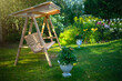 Wooden garden swing in the park with flowers. Outdoor recreation. Swing on a swing in the garden. Landscape design of a country plot.
