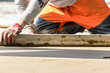 © Anoo - Close up of man builder placing screed rail on the floor covered with sand-cement mix at construction site. Male worker leveling surface with straight edge while screeding floor. Blurred background.