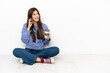 Young woman sitting on the floor holding coffee to take away and a mobile