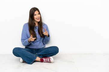 Wall Mural - Young woman sitting on the floor pointing to the front and smiling