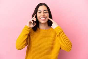 Wall Mural - Young caucasian woman using mobile phone isolated on pink background giving a thumbs up gesture