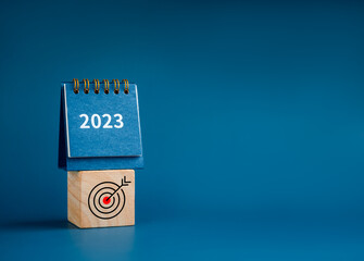 Poster - Happy new year 2023 background. 2023 numbers year on small desk calendar on wooden cube block with target icon isolated on blue background with copy space, minimalist. Ready to start a new goals.