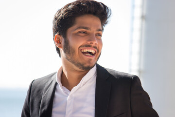 Close-up of smiling young Muslim man. Modern bearded man in black jacket and white shirt looking aside standing outdoors. Happiness and joy moments concept