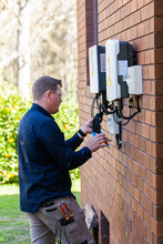 Tradie Working As An Electrician Wiring A Solar Power Control Box Beside House