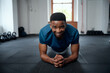 © StratfordProductions - Confident young black man in sportswear doing plank exercises at the gym