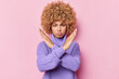 Angry sulking woman with curly hair shows taboo gesture prohibits or forbids something says enough or no dressed in knitted purple jumper isolated over pink background. Body language concept