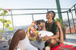 Portrait of smiling African gay men sitting on floor. Two bearded men dating one man sitting and his boyfriend lying on his knees with flowers both hugging laughing. Same sex couples love concept