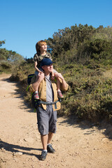 cheerful boy travelling piggyback with his father. boy hiking with son in mountains on weekend. acti