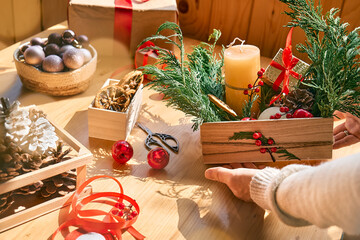 Wall Mural - Woman's hands making christmas arrangement. Female florist creating winter ikebana with fresh pine branches, candle and christmas decorations. Small business. Seasonal winter workshop.