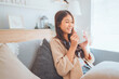 © oatawa - Joyful young asian female enjoying a cup of coffee while sitting on the the sofa at home, Cosy scene, Smiling pretty woman drinking hot tea in winter.