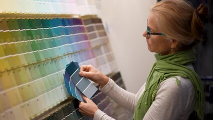 Wall Mural - Slow motion of mature woman looking at paint chips in a hardware store. Concept of shopping experience for home improvement.