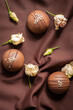 Chocolate mousse cakes on dark brown background with white flowers. Pastry dessert covered with chocolate glaze, decorated with roses and nuts on silk fabric. Modern confectionery, cafe, bakery menu