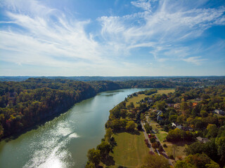 an aerial shot of a gorgeous autumn landscape along the silky green waters of the Tennessee River surrounded by autumn colored trees and lush green trees with blue sky and clouds at Sequoyah Park