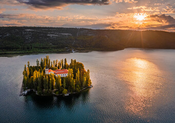 Wall Mural - Visovac, Croatia - Aerial panoramic view of Visovac Christian monastery island in Krka National Park on a sunny autumn morning with dramatic golden sunrise and clouds and clear turquoise blue water