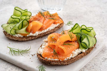 Wall Mural - Rye bread open sandwiches with salted salmon and cucumber on a white stone table. Healthy food.