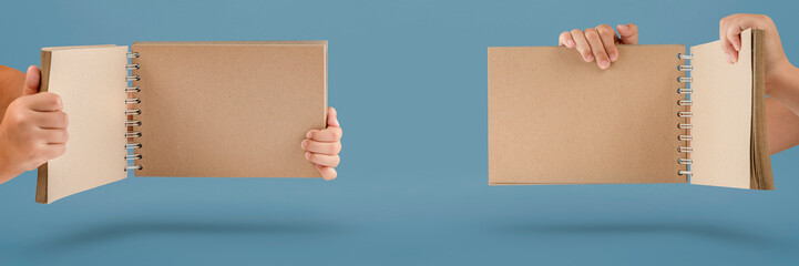 Wall Mural - Notepad in hand. Blank notepad in the hands on a blue background. Hands hold a book without text. The girl is holding a book with an empty cover.