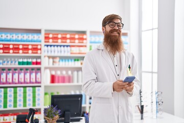 Poster - Young redhead man pharmacist using smartphone working at pharmacy