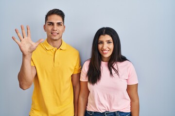 Canvas Print - Young couple standing over isolated background showing and pointing up with fingers number five while smiling confident and happy.