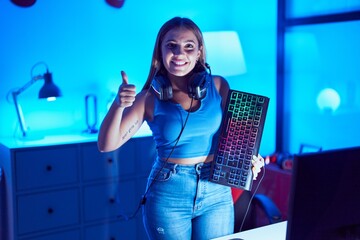 Canvas Print - Young blonde woman playing video games with smartphone holding keyboard smiling happy and positive, thumb up doing excellent and approval sign