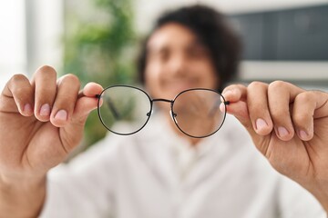 Wall Mural - Young hispanic man optician holding glasses at clinic