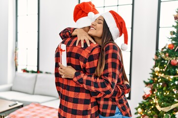 Sticker - Young latin couple smiling happy and hugging holding christmas gift at home.