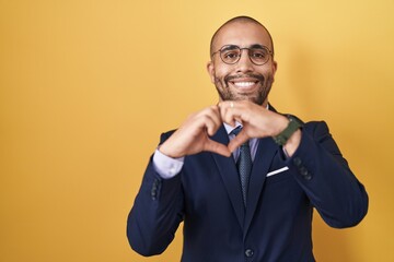 Poster - Hispanic man with beard wearing suit and tie smiling in love doing heart symbol shape with hands. romantic concept.