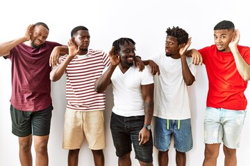 Poster - Young african group of friends standing together over isolated background smiling with hand over ear listening an hearing to rumor or gossip. deafness concept.