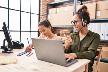 Wall Mural - Young mother and daughter working at the office and doing homework pointing thumb up to the side smiling happy with open mouth