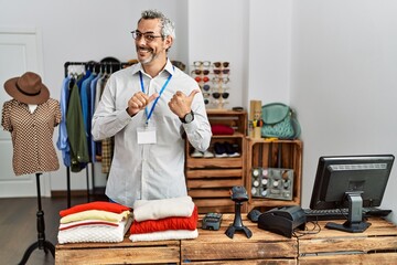 Poster - Middle age hispanic man working as manager at retail boutique pointing to the back behind with hand and thumbs up, smiling confident