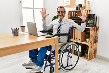 Wall Mural - Middle age hispanic man working at the office sitting on wheelchair showing and pointing up with fingers number eight while smiling confident and happy.