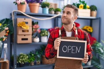 Sticker - Young caucasian man working at florist holding open sign smiling looking to the side and staring away thinking.