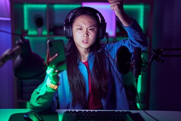 Poster - Young asian woman playing video games with smartphone angry and mad raising fist frustrated and furious while shouting with anger. rage and aggressive concept.