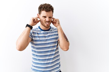 Poster - Handsome young man standing over isolated background covering ears with fingers with annoyed expression for the noise of loud music. deaf concept.